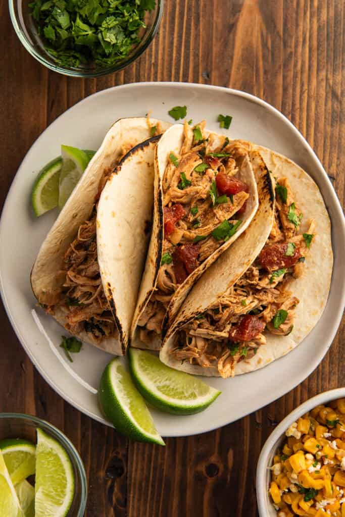 Slow cooker chicken tacos on a plate with limes
